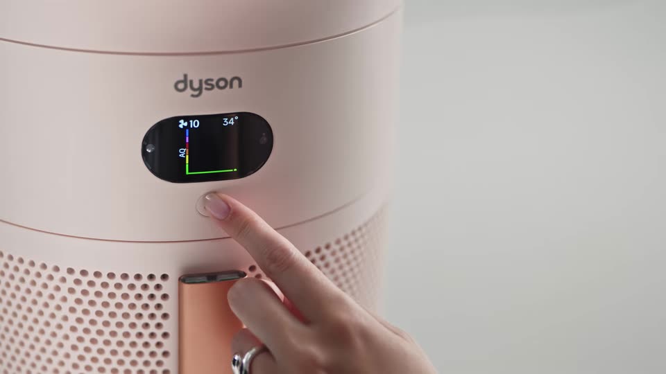 A finger pressing the button under the HushJet Hot Cool Pure+ display, which shows the live air quality graph